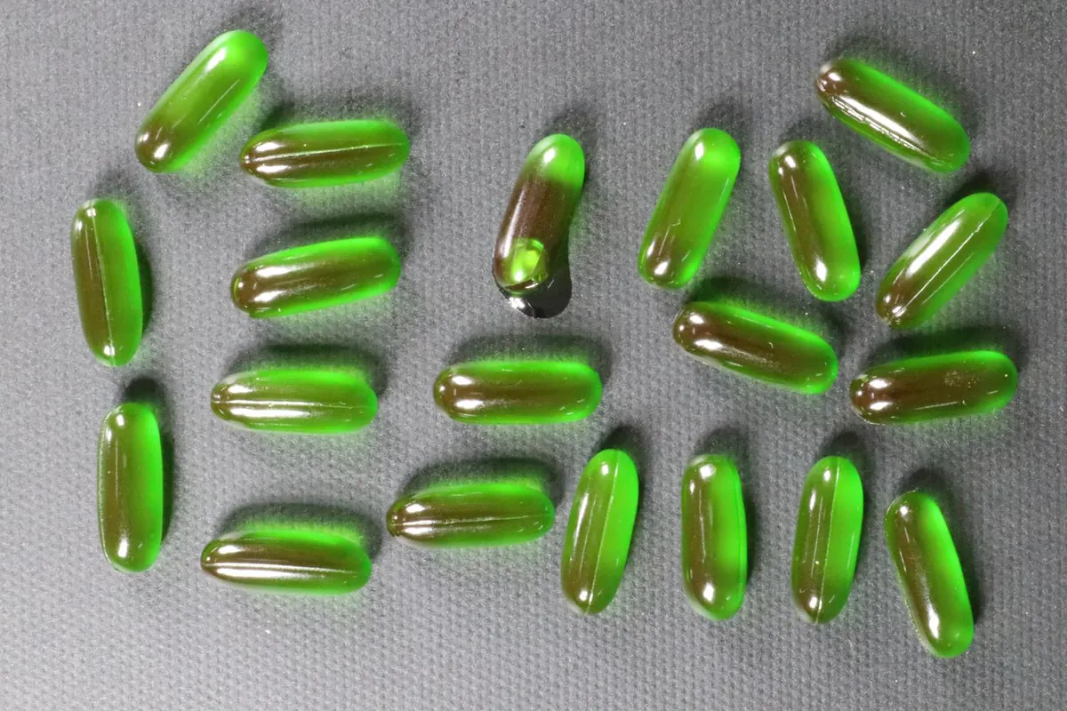 A tray of green gel capsules; one of them is leaking.