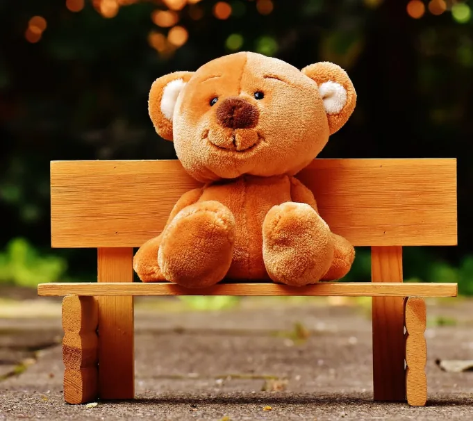 A teddy bear sitting on a wooden bench.
